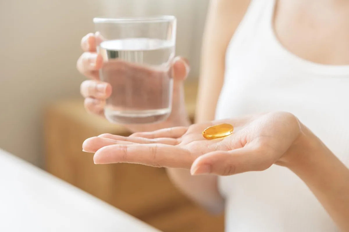 Woman holdig a supplement capsule in the palm of one hand and a glass of water in the other.