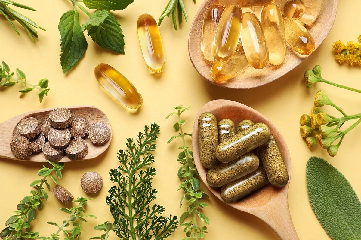 Supplement capsuls and tablets in wooden spoons surrounded by herbal ingredients.